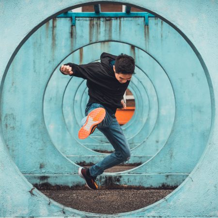 Young Asian active man in action of jumping and kicking, circle looping wall background. Extreme sport activity, parkour outdoor free running, or healthy lifestyle concept